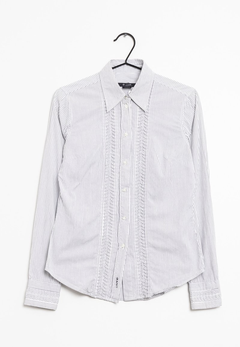 Chemise blanche à manches longues boutonnée avec fines rayures verticales noires et plis décoratifs, présentée sur un cintre noir sur fond blanc.