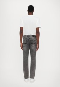 Hallid denim teksad sirge sääre lõikega, tagakottide ja valgete õmbluste aktsentidega. Kombineeritud tavalise valge t-särgiga.