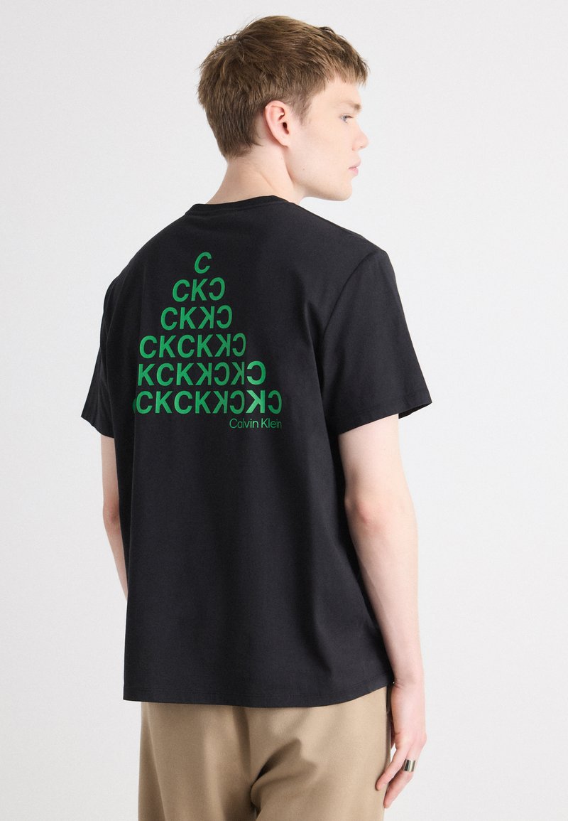 Svart bomull T-skjorte med grønn grafisk design på baksiden, som viser gjentatte bokstaver og merkevarenavnet "Calvin Klein" nederst.