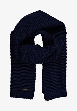 Écharpe en tricot bleu marine avec une texture côtelée épaisse, forme rectangulaire, design plié en boucle et petite étiquette noire portant l'inscription "SELECTED HOMME".