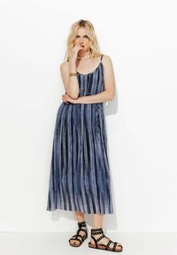 Robe midi avec des rayures verticales bleu et noir, fabriquée en tissu léger. Elle possède des fines bretelles et un design décontracté et fluide. Sandales noires à lanières.