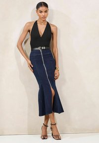 Čierny halter bodysuit v kombinácii s tmavými džínsovými sukňami s predným zipsom a bočnými rozparokmi. Čierny opasok a sandále na opätku dotvárajú vzhľad.