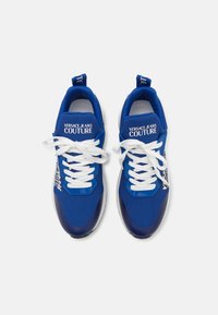 Zapatillas de malla azules con cordones blancos, que presentan un acento azul brillante y un logo impreso en el costado. Suela acolchada para mayor comodidad.