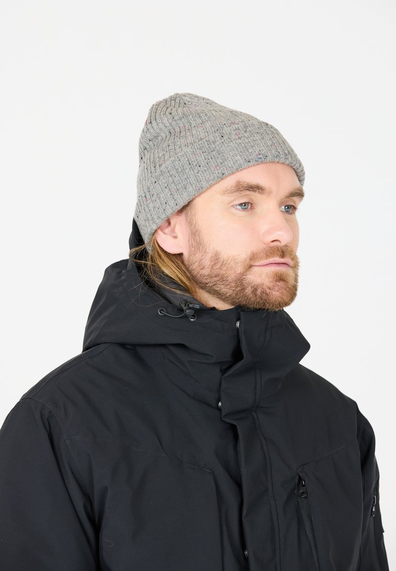 Grau gestrickte Mütze mit geripptem Muster und bunten Sprenkeln. Getragen mit einer schwarzen Zip-Jacke mit hohem Kragen und mehreren Taschen.