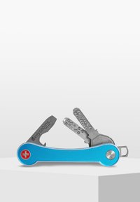 Multiverktyg med en blå aluminiumkropp. Har en silverf ärgad kniv, två metallnycklar och en rund röd detalj med ett vitt kors.
