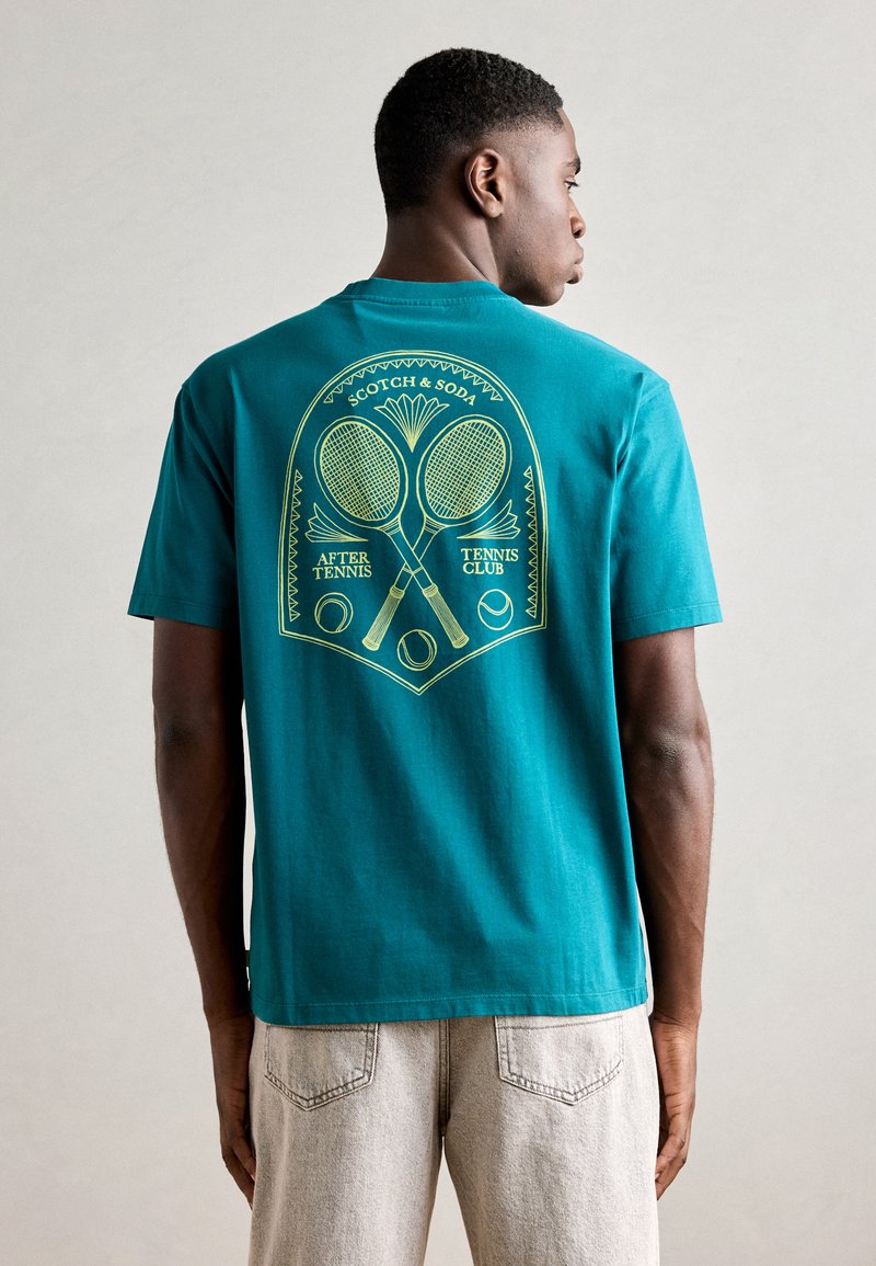 Teal bomulds t-shirt med et gult grafisk motiv af tennisrackets og bolde på ryggen, med en lige kant og korte ærmer.