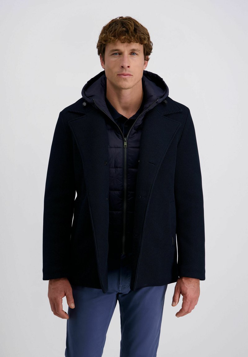 Marineblauer Mantel mit Rippstruktur, knöpfbarem Vorderteil, breiten Revers und einer Kapuze im Innenbereich. Mit einem Reißverschluss und seitlichen Taschen ausgestattet.