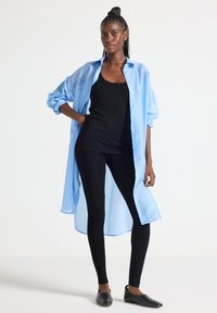 Ljusblå oversize skjorta med knappar, svart linne, svarta leggings och svarta slip-on skor. Slätt tyg, avslappnad passform och långa ärmar.