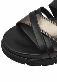 Schwarze und bronzefarbene Leder-Sandale mit mehreren überlappenden Riemen, einer strukturierten Oberseite und einer dicken schwarzen Sohle mit einem Profilmuster.