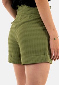 Shorts verts texturés avec une taille ajustée, un ourlet roulé et des poches latérales. Le tissu présente un motif en grille, ajoutant un intérêt visuel.