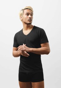 Czarny t-shirt z dekoltem w serek, wykonany z miękkiej tkaniny, dopasowany krój. Model ma również na sobie czarne bokserki, stojąc na tle jednolitego białego tła.