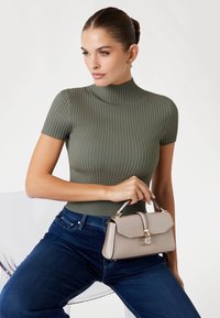 Top a maniche corte a coste color oliva abbinato a jeans blu scuro. Una borsa beige chiaro presenta un design strutturato e dettagli in hardware dorato.