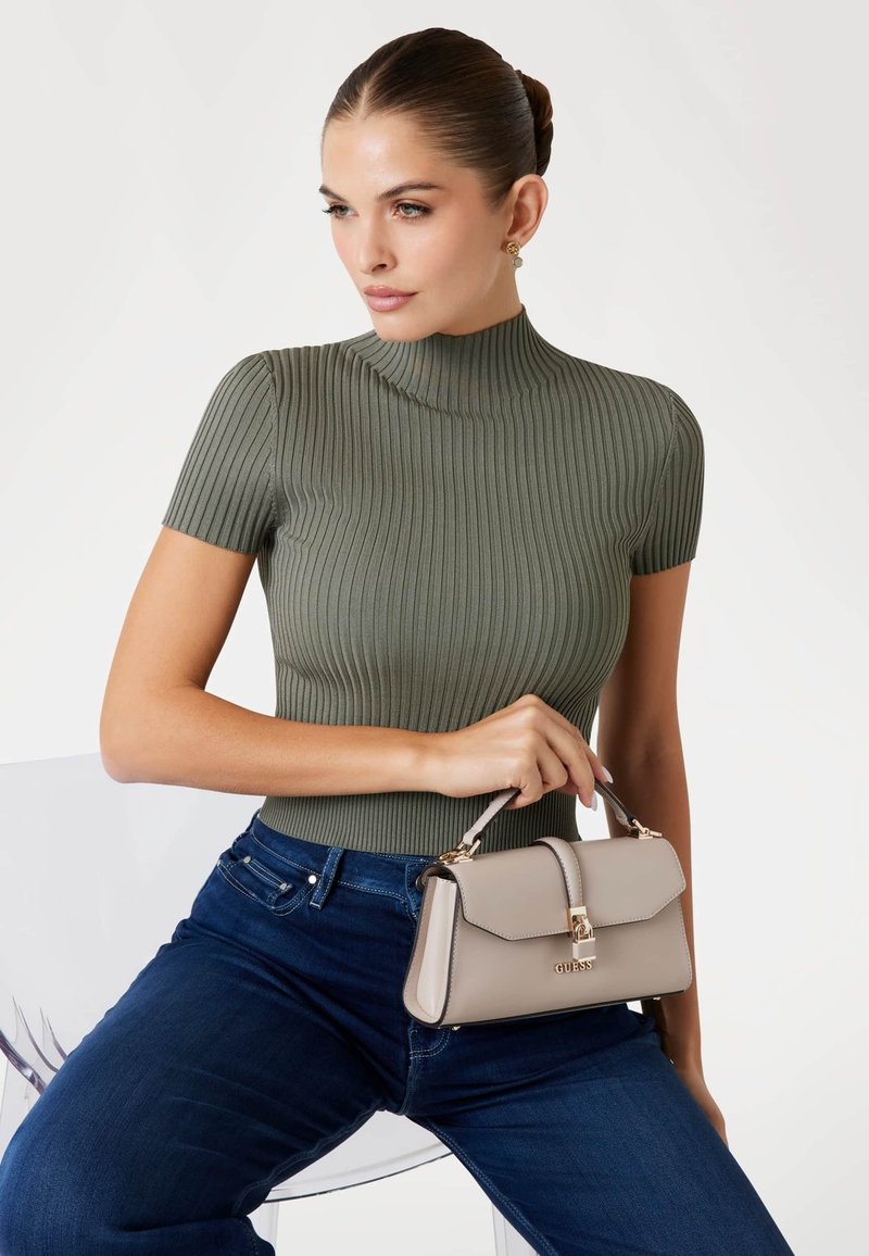 Top a maniche corte a coste color oliva abbinato a jeans blu scuro. Una borsa beige chiaro presenta un design strutturato e dettagli in hardware dorato.