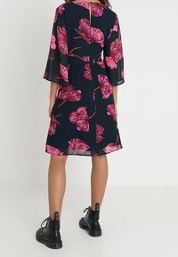 Bloemendress met een donkerblauwe achtergrond en grote roze bloemenpatronen, doorzichtige mouwen, A-lijn snit en een sleutelgatdetail aan de achterkant.