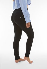 Leggings neri con una texture liscia e un design aderente, caratterizzati da tasche posteriori e un accento in metallo con il logo. Completati da un top azzurro chiaro.