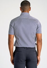 Camicetta a maniche corte a quadri blu e bianca, con colletto rigido e vestibilità su misura. Abbinata a pantaloni blu scuro.