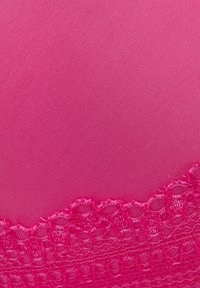 Rozā audums ar gludu, teksturētu virsmu; apakšā ir mežģīņu apdare, pievienojot sarežģītu detalizāciju dizainam.