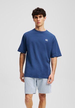 Marineblå bomulds T-shirt med rund hals, korte ærmer og et lille hvidt grafik på brystet, parret med stribede shorts.