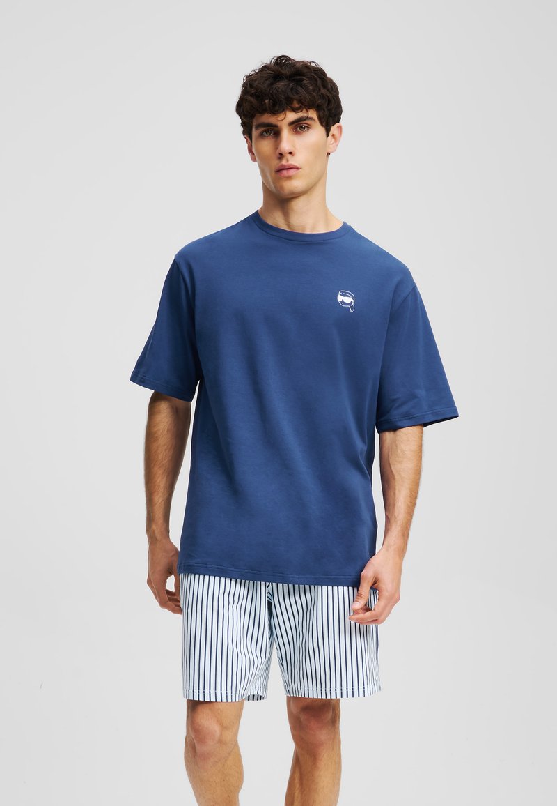 T-shirt in cotone blu navy con collo rotondo, maniche corte e una piccola grafica bianca sul petto, abbinata a pantaloni a righe.