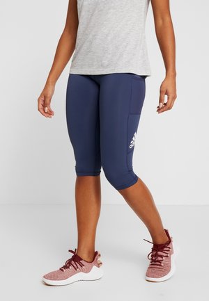 Navy atletiska capri leggings med en sidficka och vit logotyp, i kombination med strukturerade vinröda sneakers och en ljusgrå ärmlös topp.