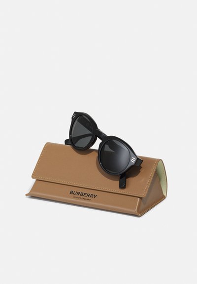 Occhiali da sole neri con lenti tonde appoggiati su un astuccio in pelle beige dotato di chiusura magnetica e marchio impresso.