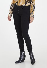 Jeans negros ajustados con cierre de cinco botones, costuras decorativas y costura de contraste. Combinados con botas de tobillo de cuña negras brillantes.