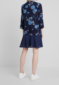 Námořnické květinové šaty s tříčtvrtečními rukávy, s modrými a bílými květinami, kulatým lemem a texturovanými vzory. Nosené s bílými teniskami.