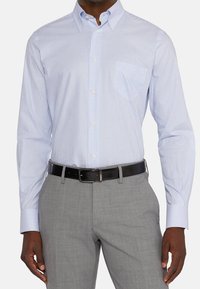 Koszula w niebiesko-białe paski na guziki z kieszenią, zestawiona z szarymi spodniami o fakturze i czarnym paskiem. Długie rękawy, kołnierzyk.