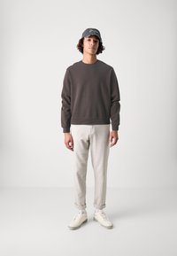 Grå sweatshirt med rund hals, lysegrå opsmøgede bukser og hvide sneakers. En mørk kasket med hvid broderi på forsiden.