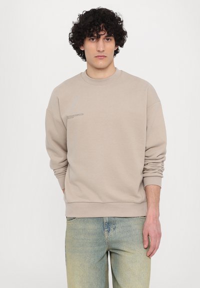 Beige sweatshirt in soft fabric, featuring a round neckline and ribbed cuffs. Text printed on the front adds detail to the minimalist design.