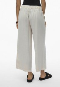 Pantaloni larghi beige chiaro con vita elastica, realizzati in un tessuto morbido e leggero. Abbinati a sandali neri in tessuto testurizzato.