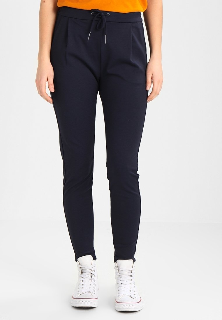 Pantalones jogger en color navy con cintura ajustable, dos bolsillos frontales y un diseño de pierna tapered, combinados con zapatillas altas blancas.