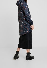 Impermeabile floreale blu navy con motivi a fiori rossi e blu, maniche lunghe e cappuccio. Abbinato a una gonna nera alla caviglia e stivali neri.