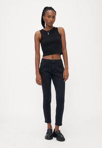 Fekete rövidített tank top sötét szűk farmernadrággal kombinálva. Az öltözet elegáns megjelenéssel bír, sima textúrával és látható minták nélkül.