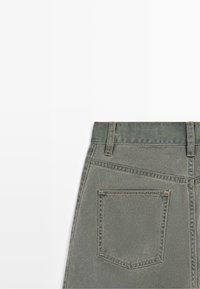 Vue arrière d'une jupe en jean grise montrant la taille avec passants de ceinture et une poche arrière rectangulaire unique avec des coutures visibles.