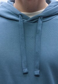 Sweatshirt azul com capuz, feito de tecido macio, apresentando um logotipo frontal, cordões com design texturizado e corte descontraído.