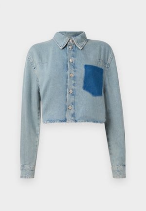 Chaqueta de mezclilla azul claro, corta, con mangas largas, botones plateados en el frente y un bolsillo de parche azul oscuro en el lado izquierdo del pecho.
