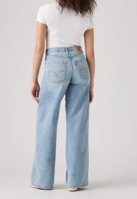 Ljusblå denim bredbenta jeans med hög midja, synliga bakfickor och en läderlogotyp på midjebandet.