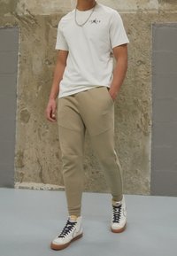 Vit t-shirt med svart "JORDAN"-grafik, ihop parat med beige sweatpants. Tillbehör inkluderar en silverkedja och vita/tan h ög-top sneakers.