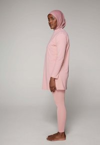 Lichtroze tuniek met lange mouwen en hoge halslijn, gecombineerd met bijpassende leggings. Zachte, gladde stof, gesneden in een ontspannen pasvorm.