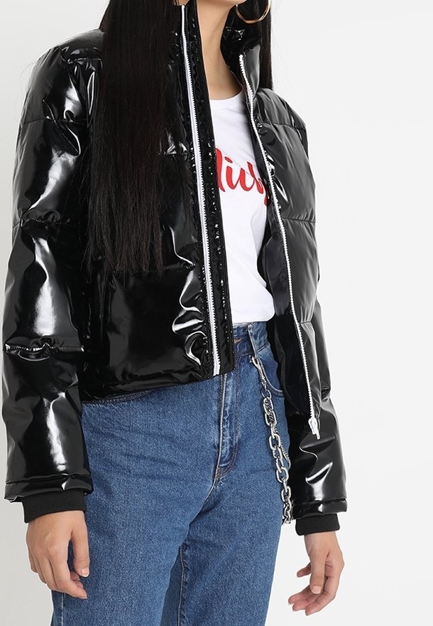 Czarna, błyszcząca kurtka puchowa na suwak, z ściągaczami przy rękawach i krótszym fasonem, zestawiona z białym t-shirtem z nadrukiem i niebieskimi jeansami.