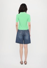 Short-sleeved, mint green polo shirt with white trim paired with loose-fitting, blue denim shorts. Smooth texture, casual design.