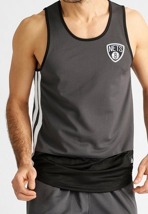 Man met een grijze Brooklyn Nets basketbaltanktop met zwarte en witte zijstrepen en bijpassende grijze shorts.