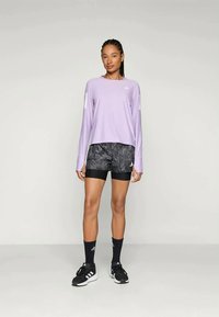 Haut de sport à manches longues violet avec une coupe décontractée, associé à un short à motifs noir et gris, et des baskets noires avec des accents blancs.