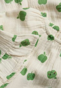Stoff mit grünem Apfelmuster, das kleine, lächelnde Äpfel auf einem cremefarbenen Hintergrund zeigt. Das Material wirkt weich und leicht mit einer gewellten Textur.