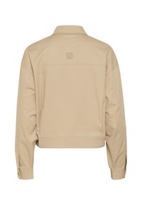 Beige cropped jakke lavet af glat stof; har en krave, lange ærmer med knapmanchetter og et logo detail på bagsiden.