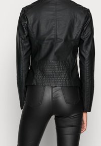 Svart läderjacka med kviltade detaljer på axlarna och ryggen, skräddarsydd passform och en slät yta. Bärs med svarta läderbyxor.