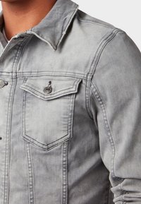 Grå denimjacka med spetsig krage, två bröstfickor med knapplock och en något blekt textur för en sliten look.