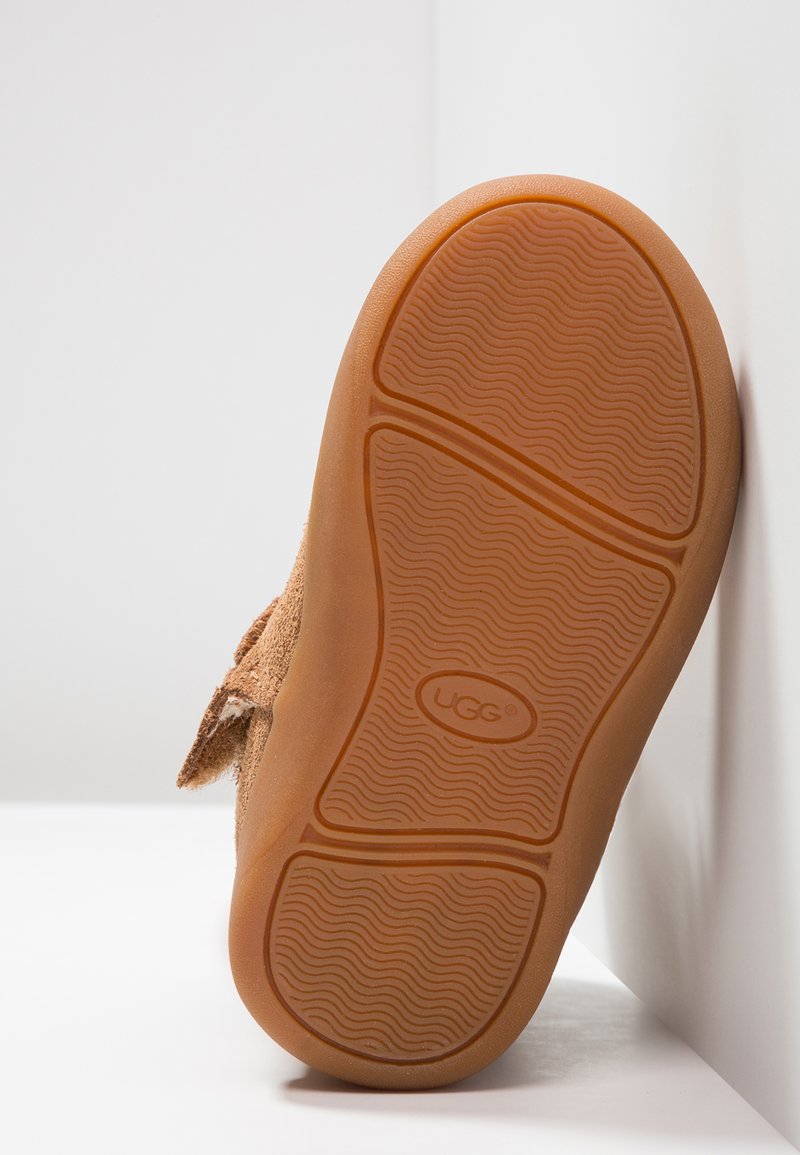 Semelle en daim brun avec caoutchouc texturé en motif ondulé ; présente un logo circulaire et un accent en boucle à l'arrière.