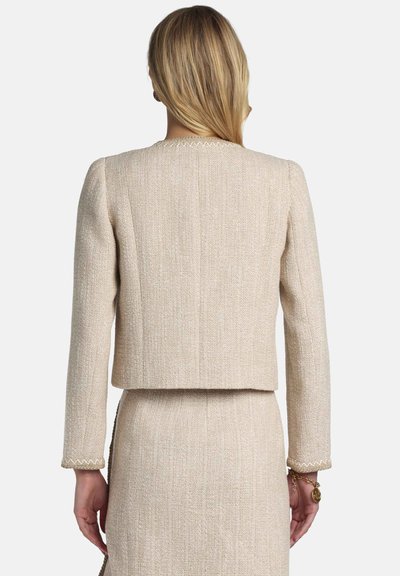 Beige tweed blazer with a cropped design, long sleeves, and a textured finish. Notable stitching detail along the cuffs and collar.